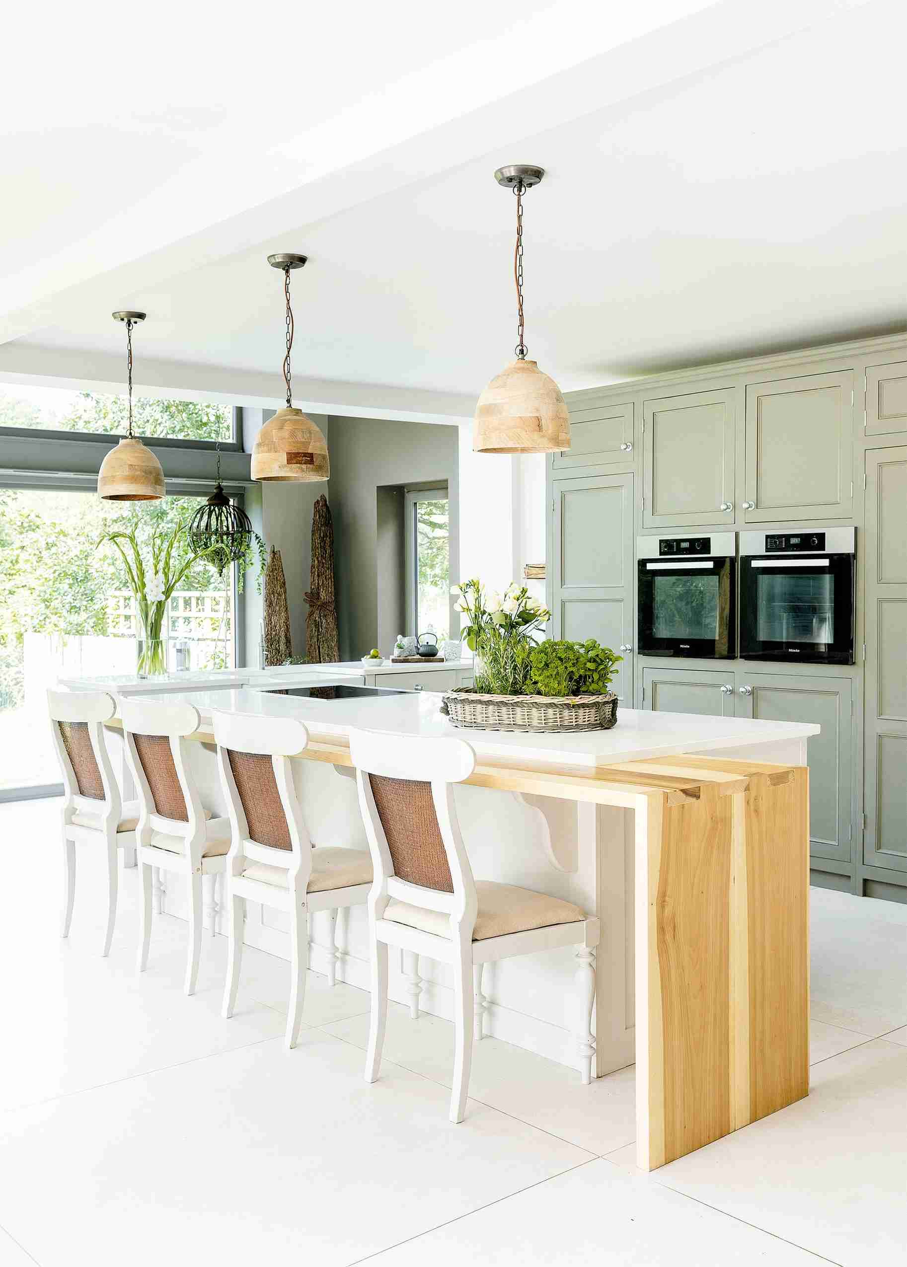 Upholstered kitchen stools at a light island with green cabinetry behind them, illustrating the fixed fabric seating discussed in the source.