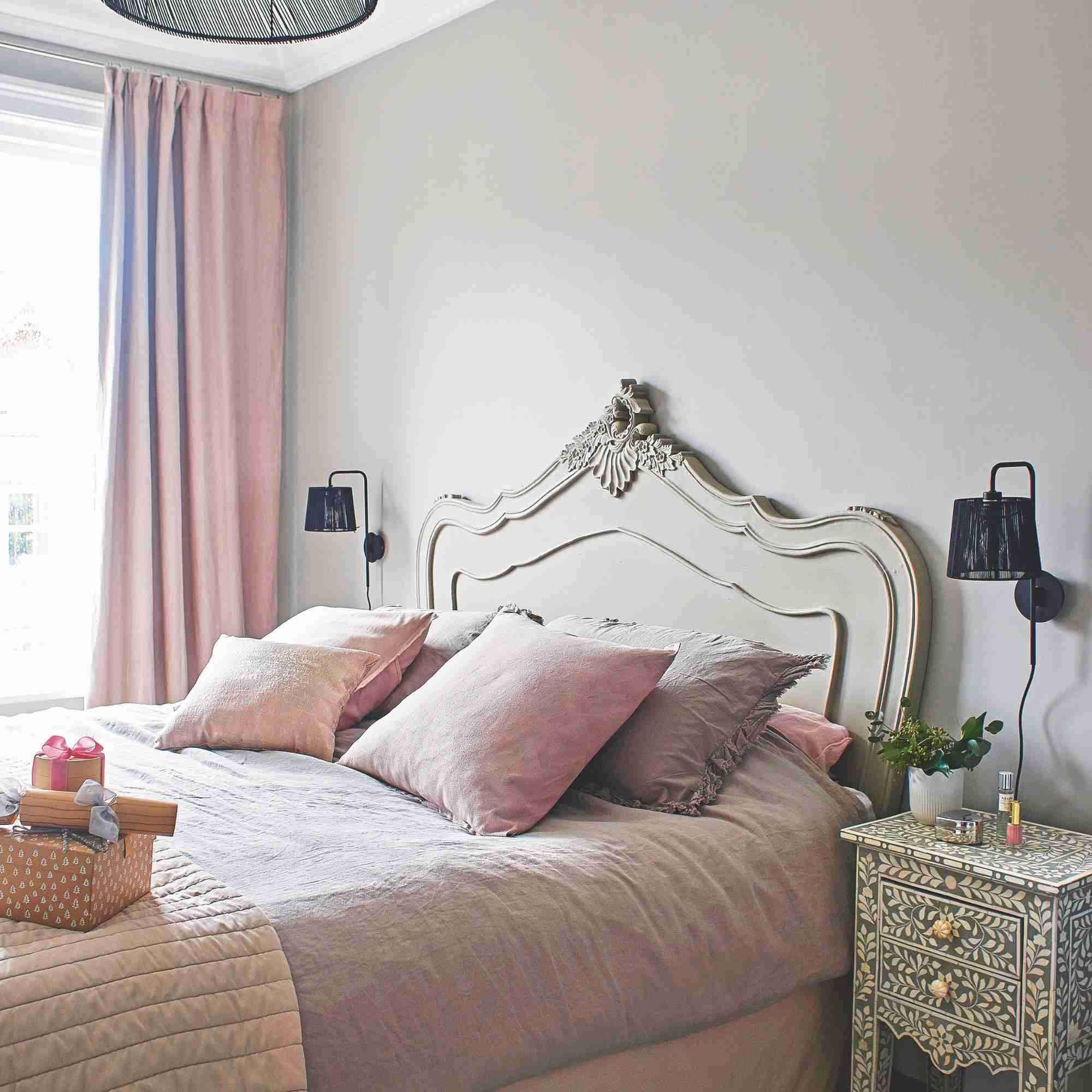 A double bed with pale pink bedding, matching cushions and a decorative headboard, illustrating the bedding discussed in the source.