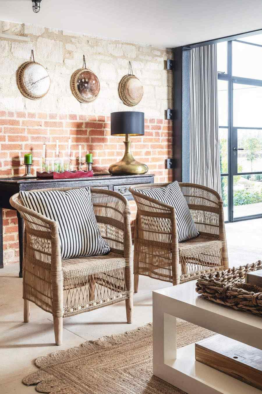Two woven armchairs in a bright interior beside an exposed-brick wall, as illustrated in the wicker-maintenance source.