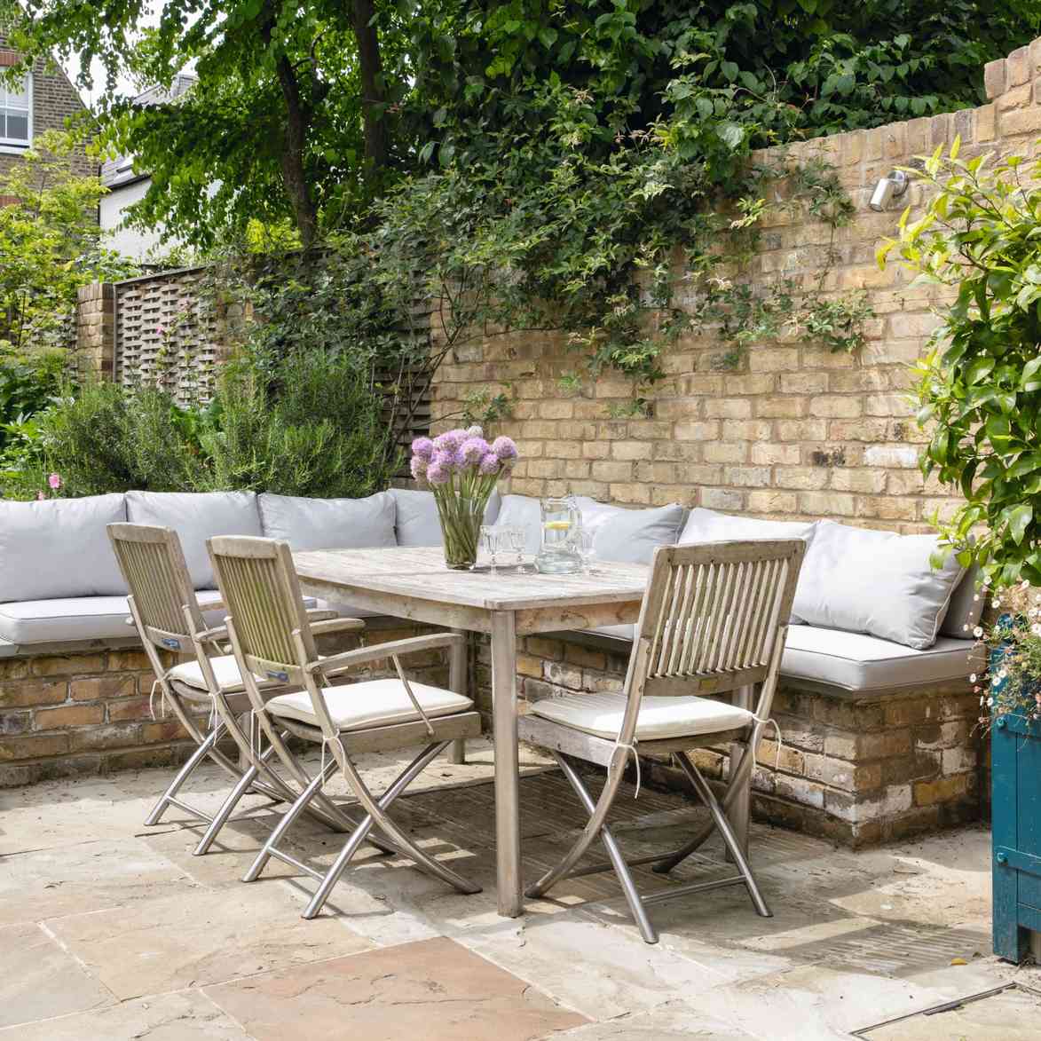 An outdoor wooden dining table and slatted chairs beside cushioned garden seating, as shown in the Ideal Home source.
