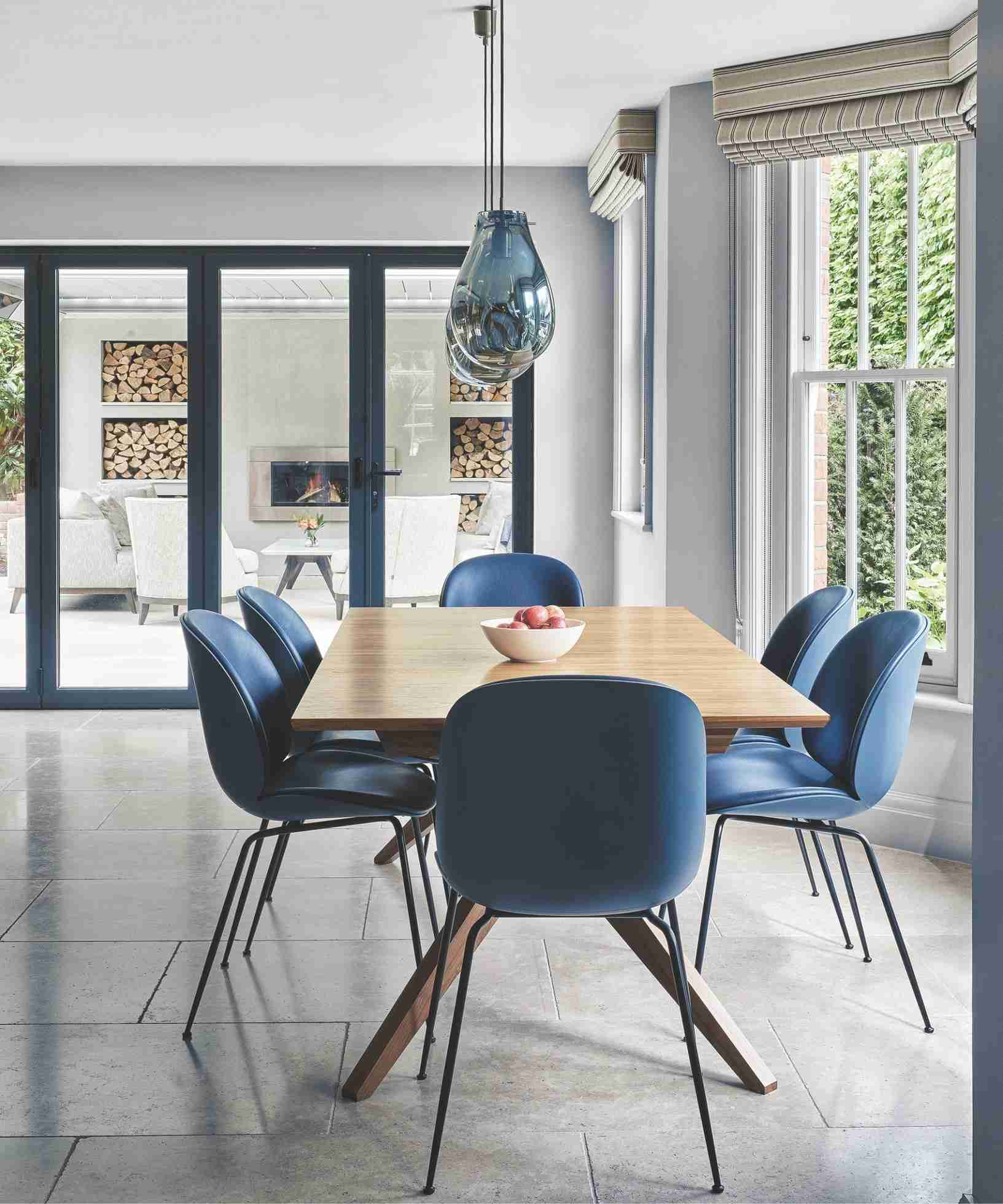 A bright dining area with large windows, a wooden table and blue chairs, used as a daylight illustration in the source window-cleaning feature.