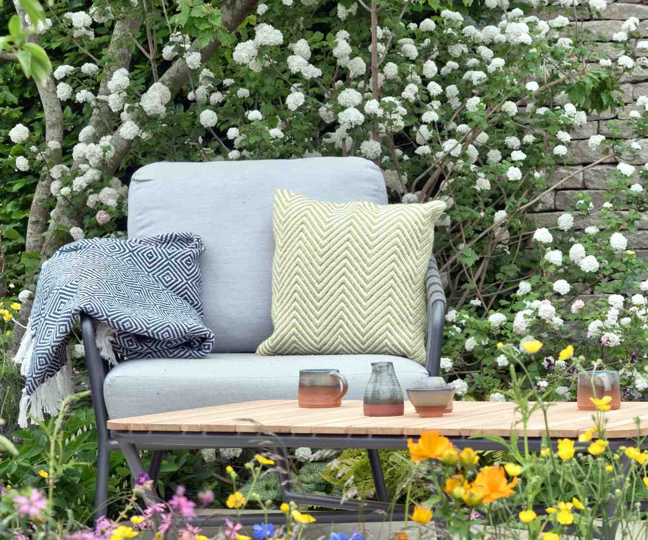 A garden armchair with cushions and a throw beside a low table, showing fabric components that need separate seasonal care.