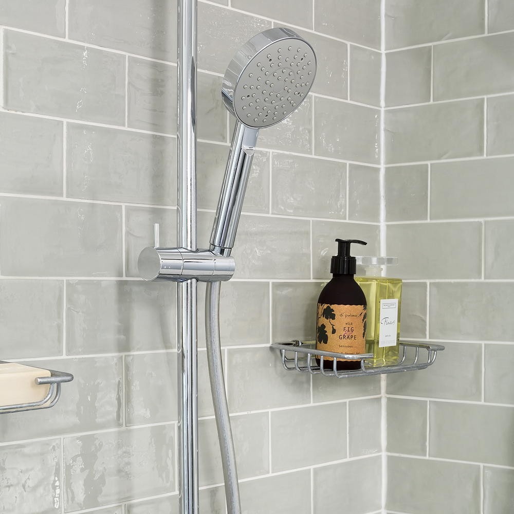 A shower corner with pale gray tiles, recessed grout lines and a small bottle shelf, illustrating the source discussion of recurring damp areas.