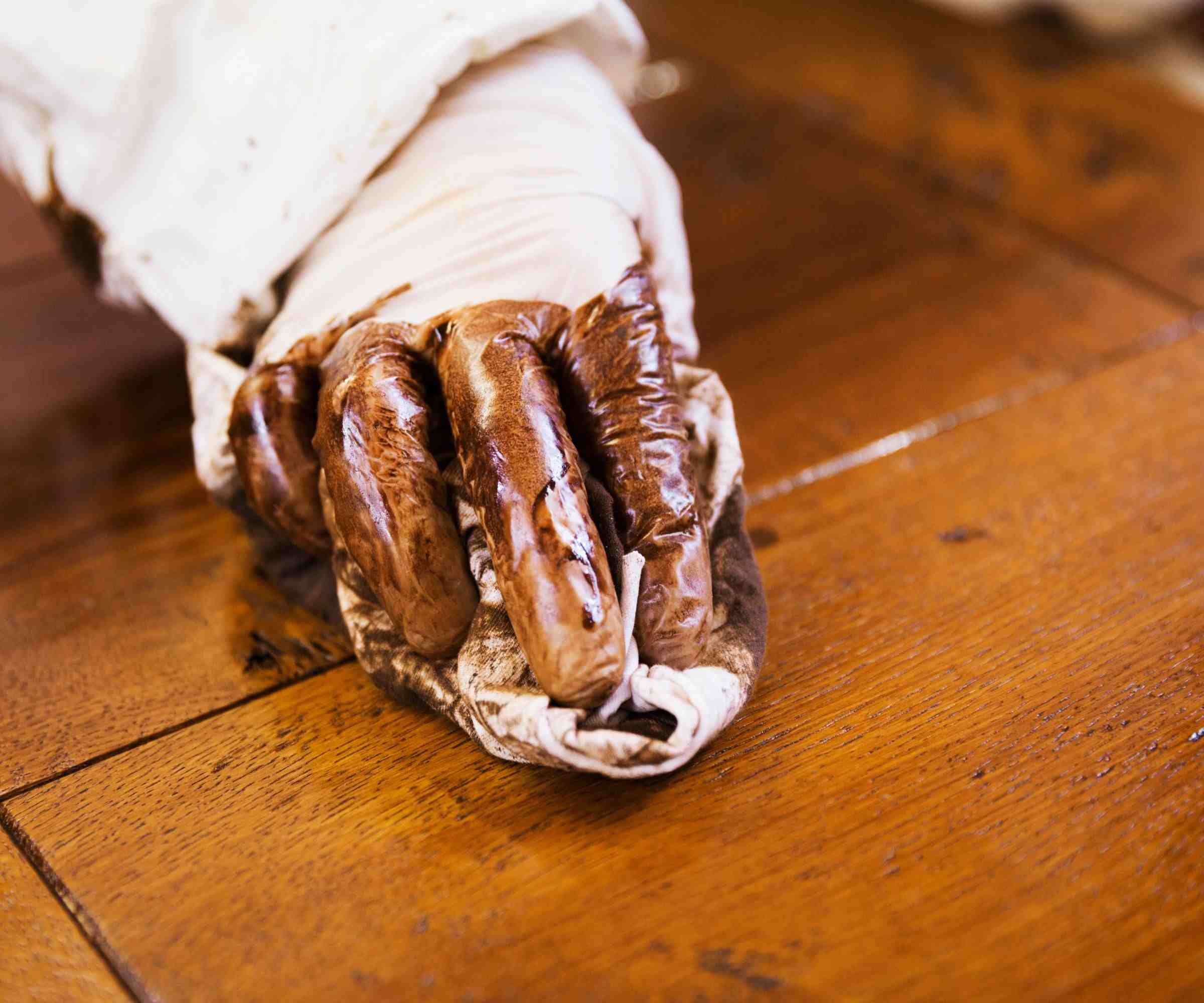 A gloved hand applying a wood treatment with a cloth along the surface, as illustrated in the source staining guide.