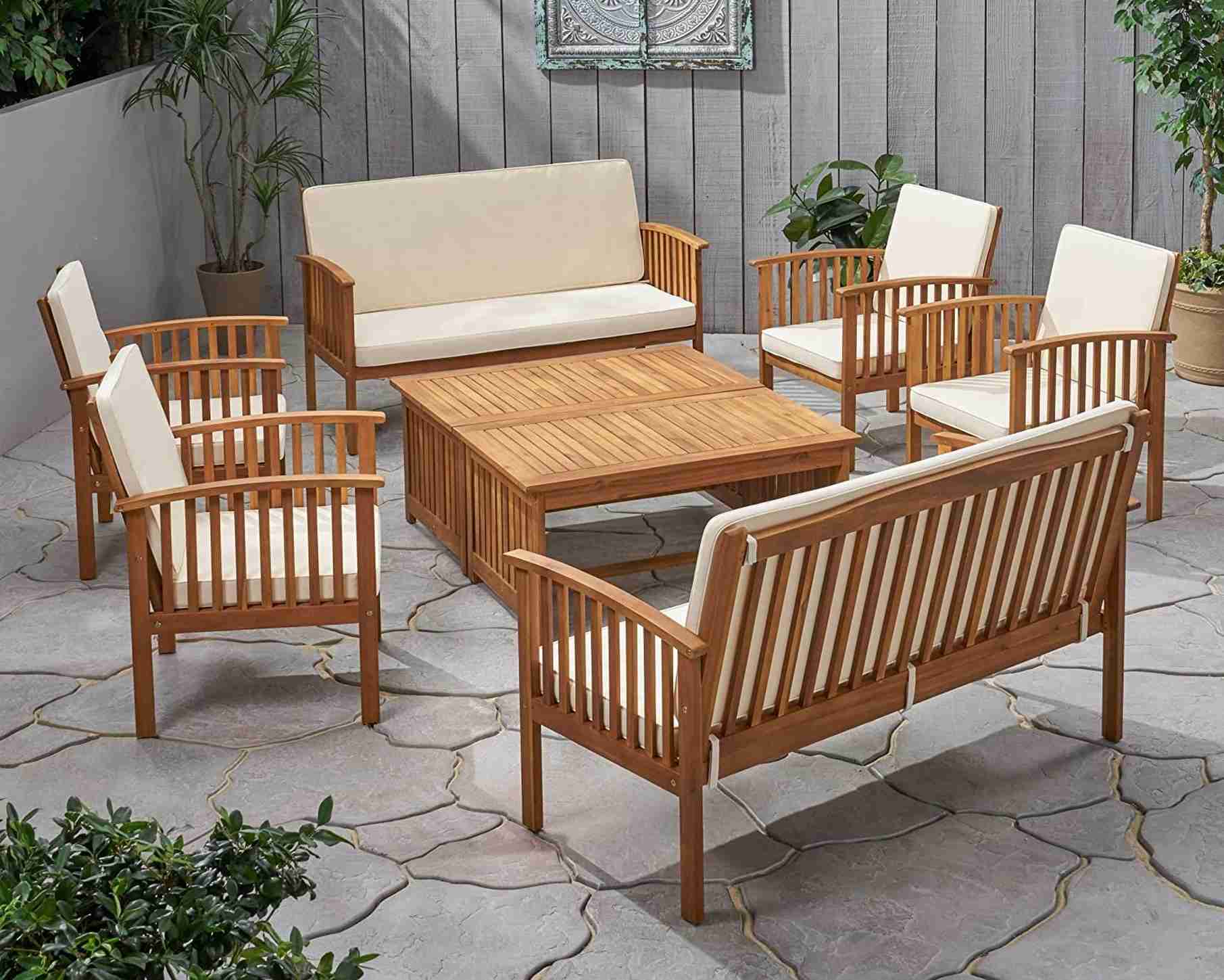 A slatted teak seating set with removable cream cushions around a matching low table, illustrating the source furniture-care topic.
