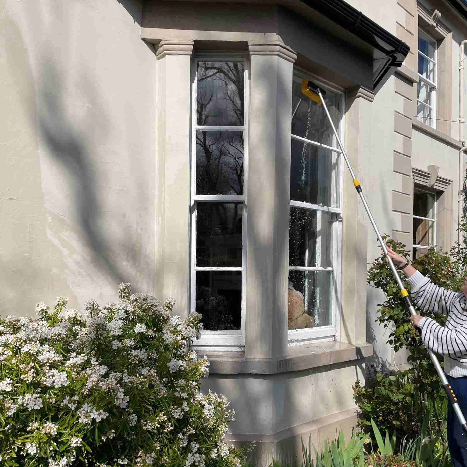 The reviewer using the extended hose-fed brush against an exterior bay-window pane in the source tool trial.