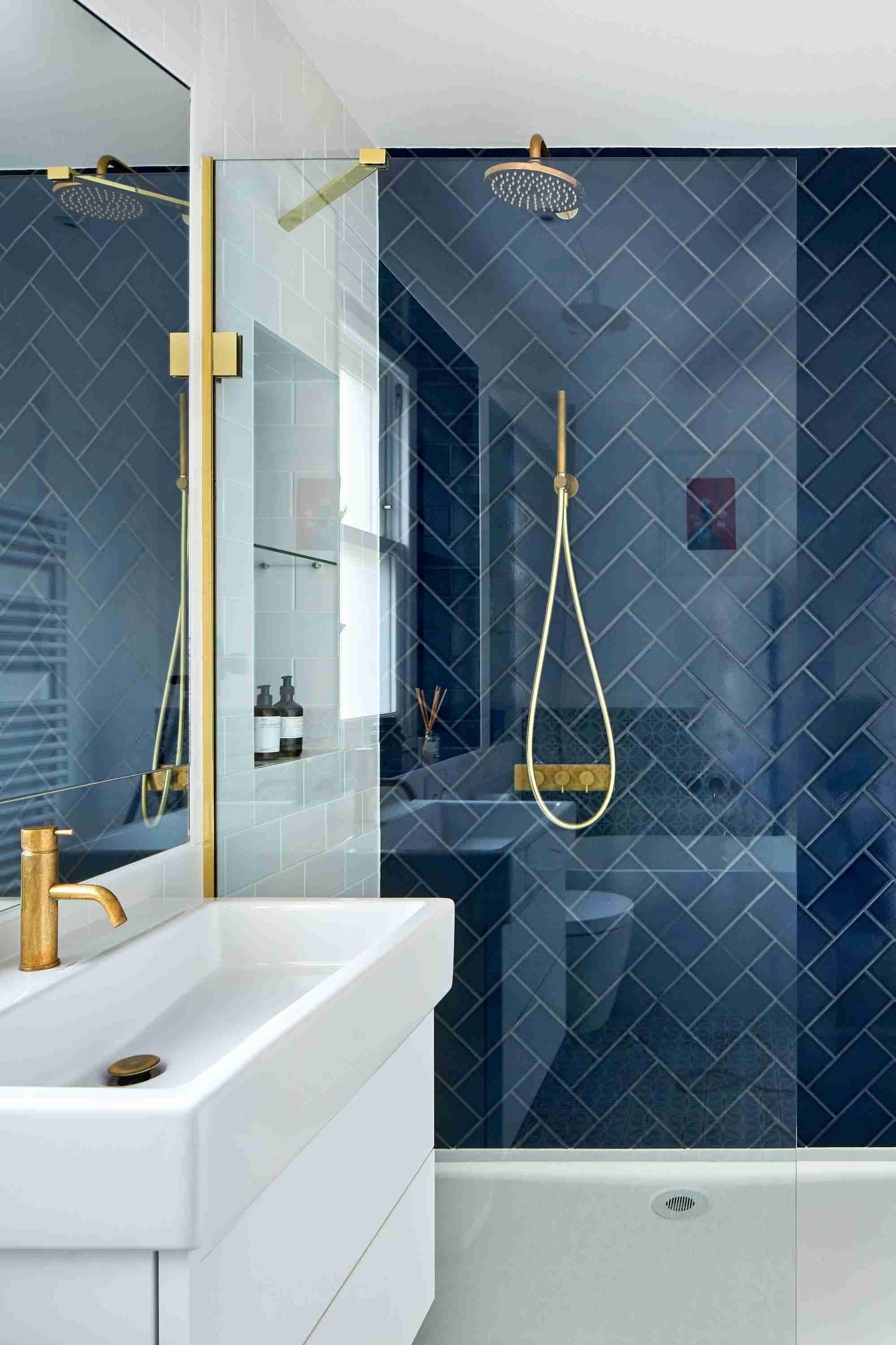 A glass shower enclosure with dark blue tiles and gold-colored fittings, illustrating the separate pane, coating and hardware care considerations.