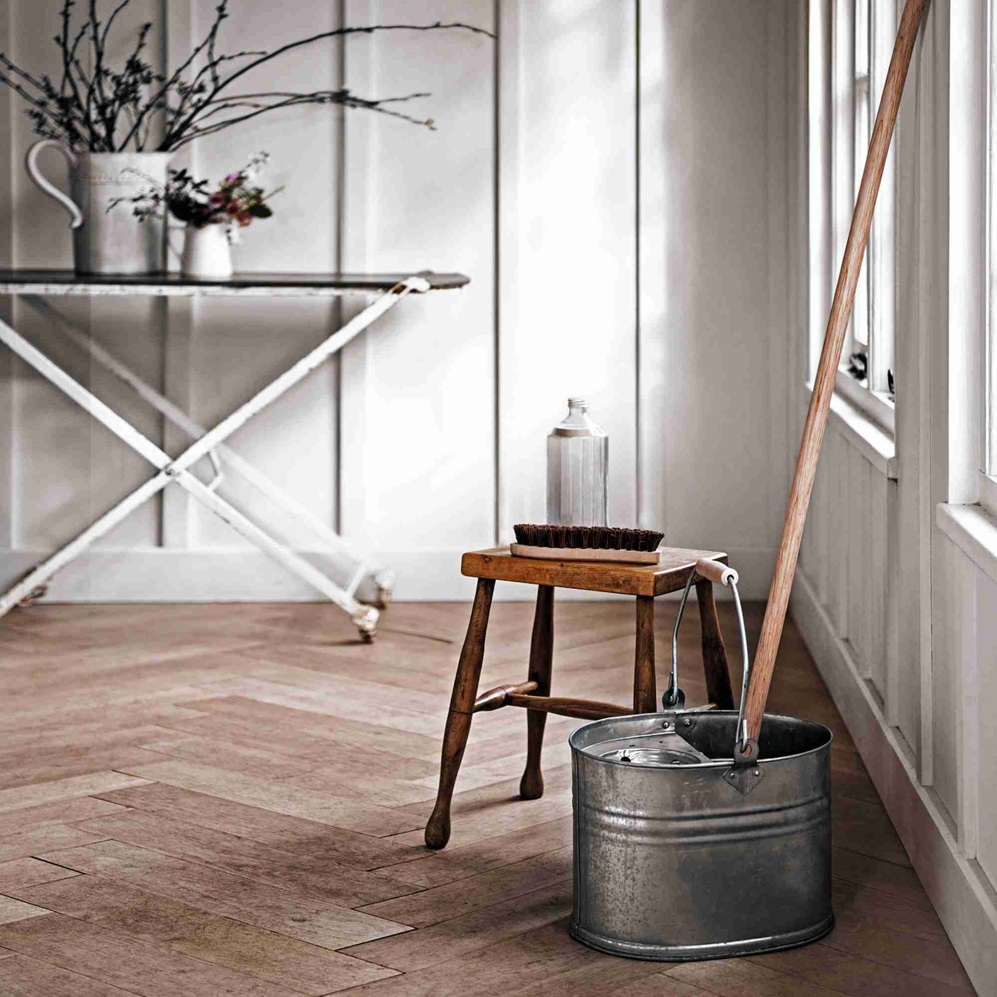 A mop and bucket standing beside a stool on a wooden floor, illustrating the source floor-maintenance topic.