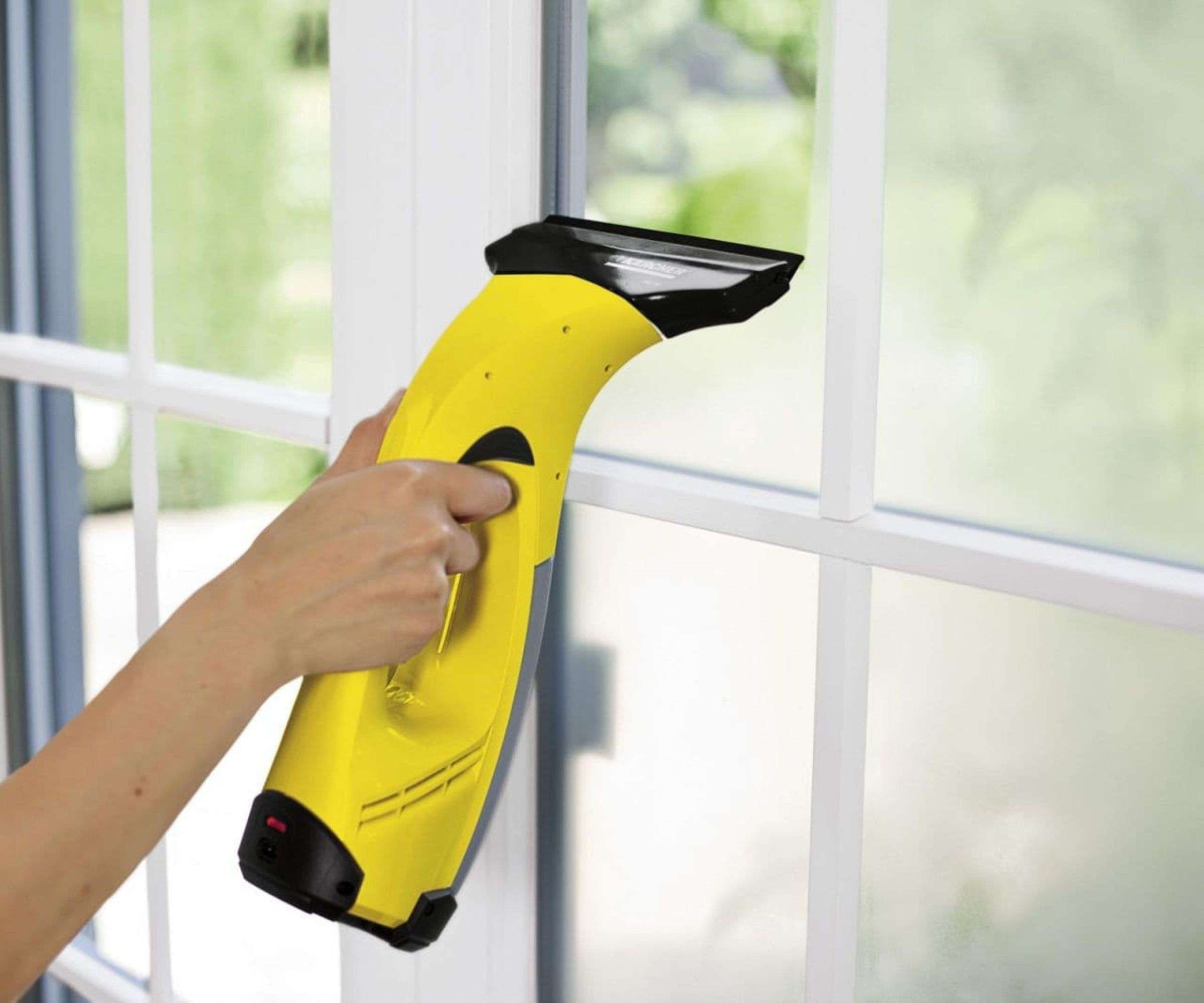 A hand guiding a yellow window vacuum along a glass pane in the source window-cleaning feature.