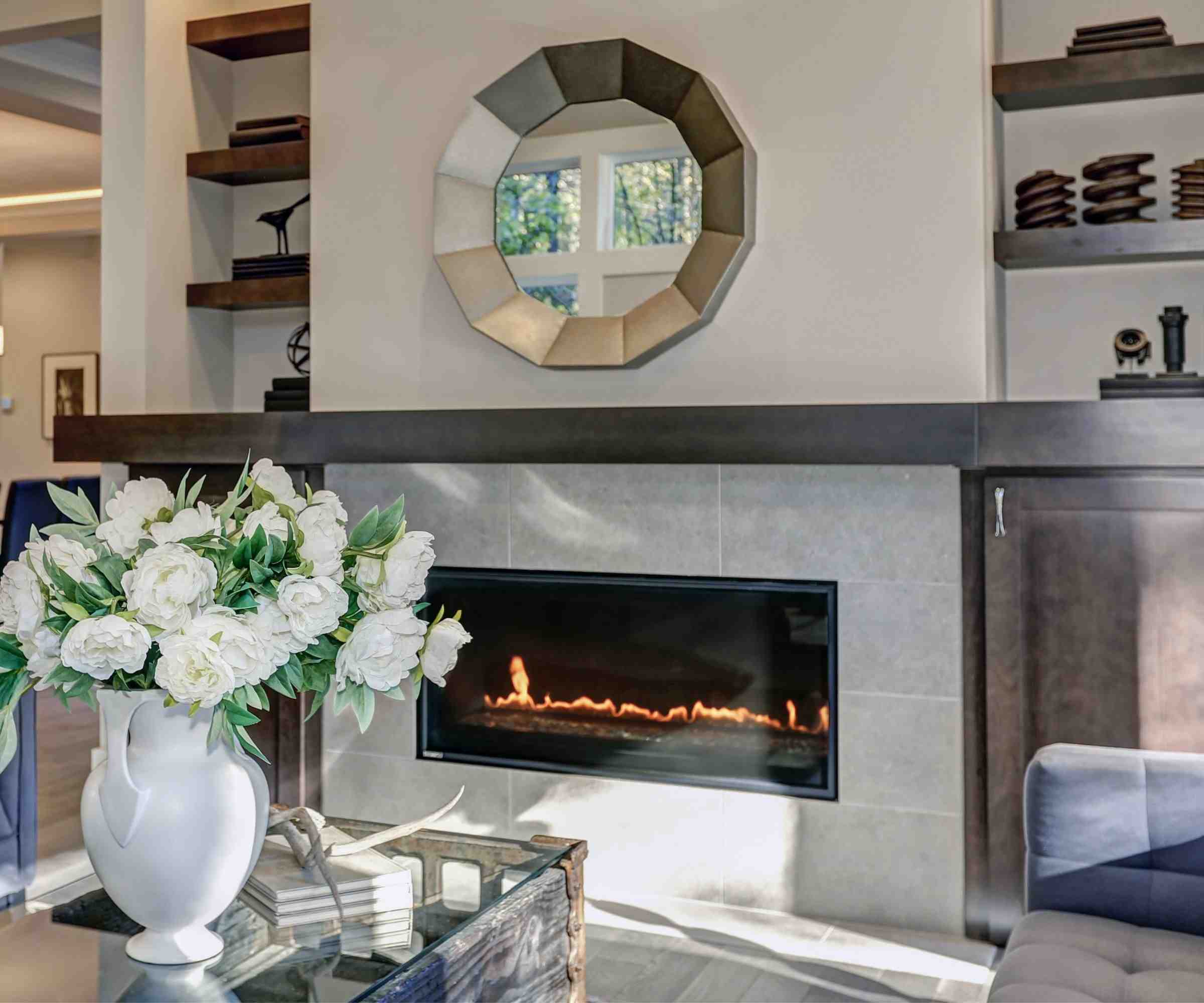 A horizontal glass-fronted gas fireplace below a mirror in a living room, illustrating the appliance discussed in the source maintenance guide.