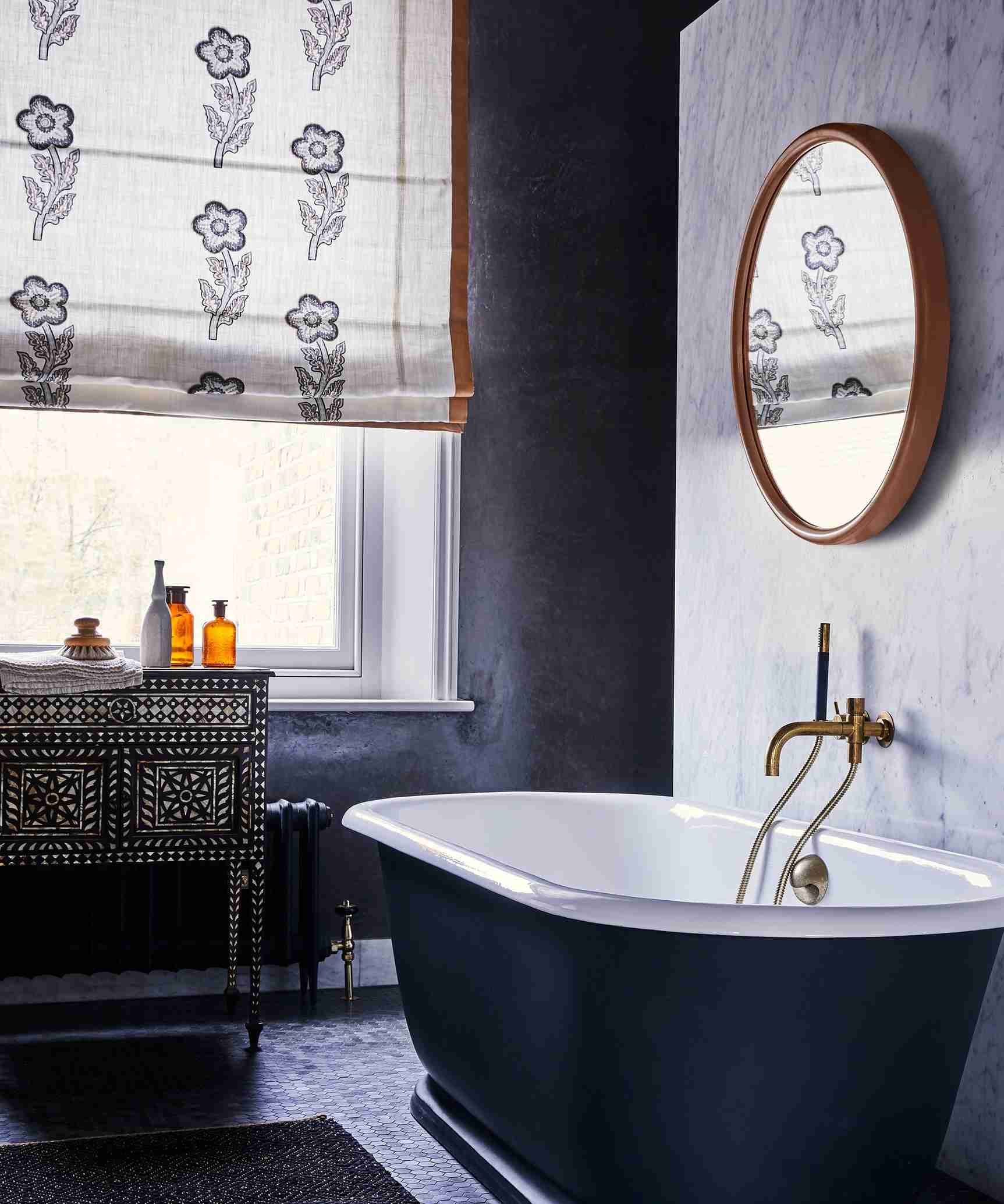A bathroom window with a patterned Roman blind beside a freestanding bath, illustrating the nearby furnishings to protect during window cleaning.
