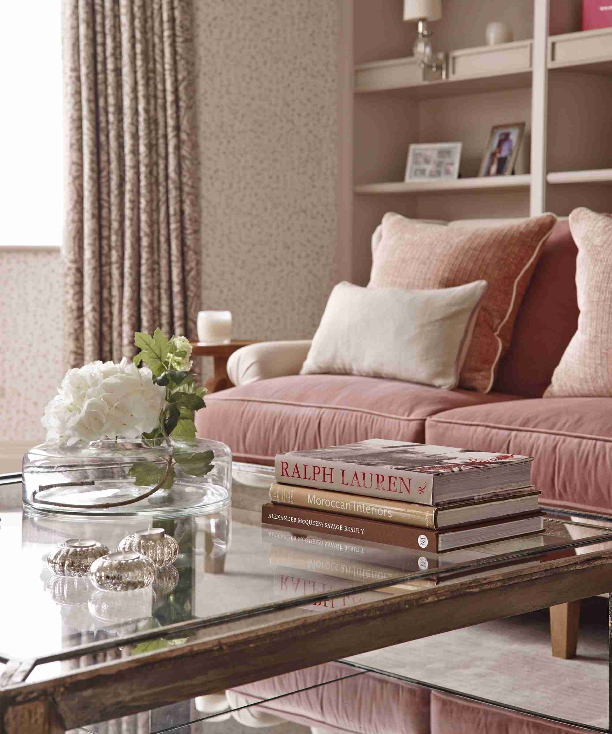 A glass coffee table with books and a flower vase in a living room, illustrating the tabletop-care subject of the source guide.